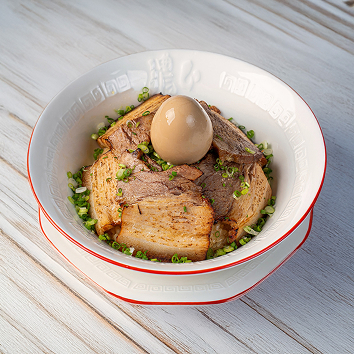 흰색 그릇에 담긴 일본식 라멘으로, 맑은 국물 위에 차슈 고기 여러 장과 반숙 달걀, 잘게 썬 파가 올려져 밝은 나무 테이블 위에 놓인 모습입니다.